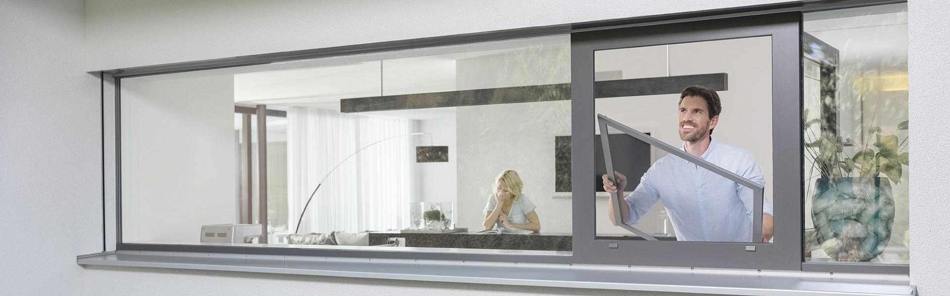 Ein Mann baut in sein Fenster ein Spannrahmen ein.